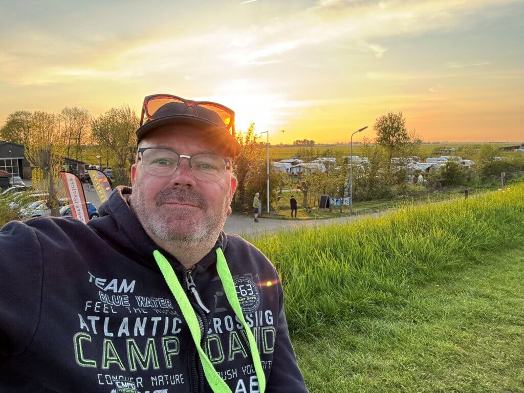 Hans van CaravanKamperen zit bovenop de dijk bij Camping de Zeevangshoeve in Edam uitkijkend op het IJSselmeer